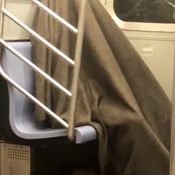 Guy sleeps under brown blanket in corner of subway
