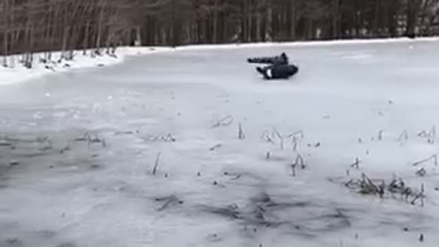 Man sleds across frozen lake in a black tube pulled by truck