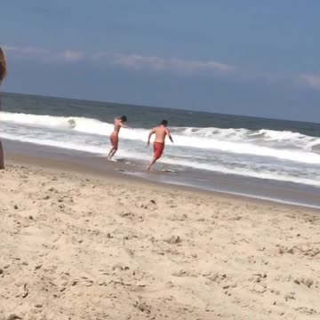 Guy red swim shorts goes into water with friend faceplants into sand water beach