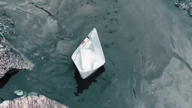 A Paper Boat Floating Over A Roadside Water Canal