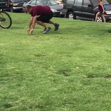 Guy maroon shirt trying to practicing standing up on surfboard park grass