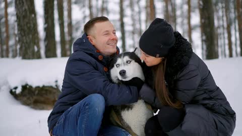 Family portrait of cute happy couple hugging with their alaskan malamute dog licking man's face