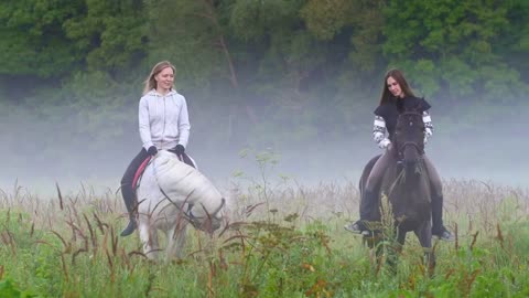 Two young girls on horseback out of the fog, talking, smiling