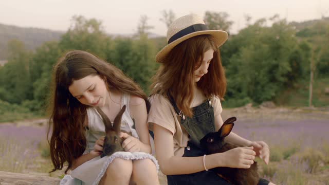 Two Girls Sitting while Holding Rabbits