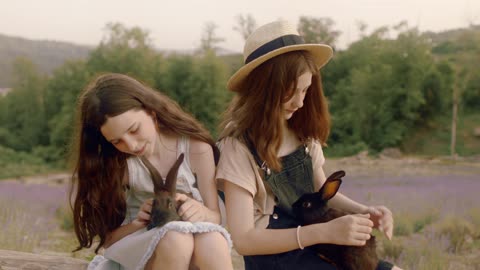 Two Girls Sitting while Holding Rabbits