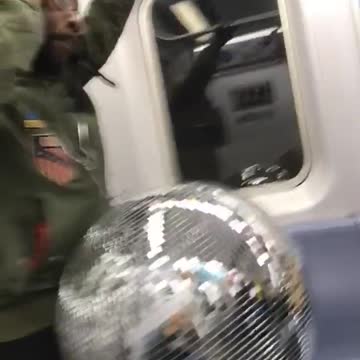 Guy holds giant disco ball on subway train