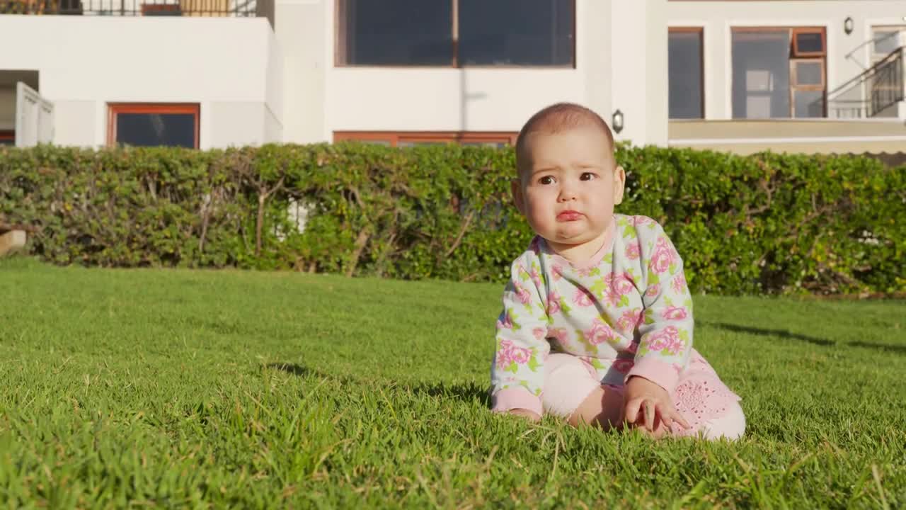 The dog runs around the little baby girl in the backyard of the house