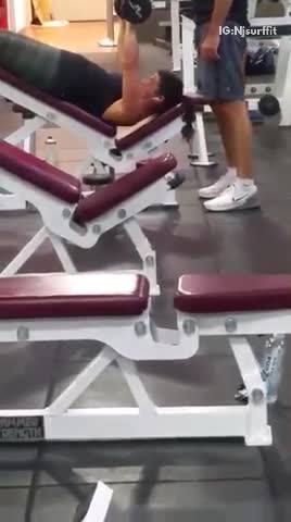 Guy on red incline bench at gym benching with free weights
