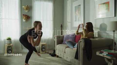 Girl with cell phone recording sister dancing in livingroom / Cedar Hills, Utah, United States