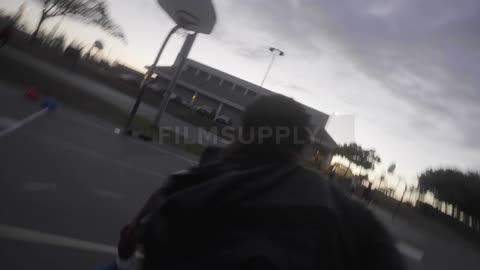Man dribbling a basketball and scoring a point on an outdoors court at evening