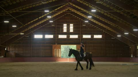 Young female equestrian horse trainer semi-silhouetted riding between open doors