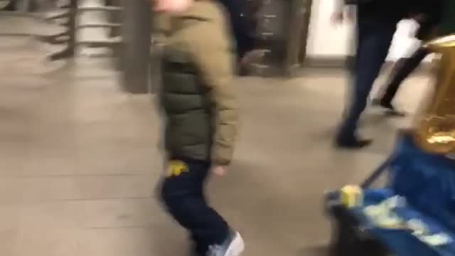 Little boy in green dancing next to street performer