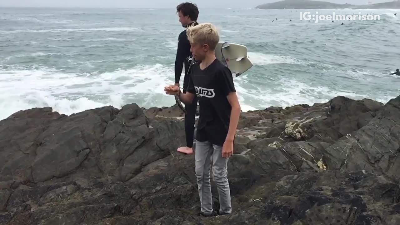 Guy in black wetsuit gets hit by wave in slomo