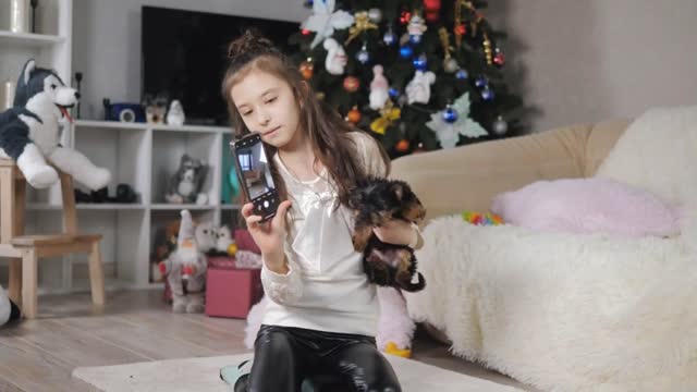 A teenage girl takes a selfie on her smartphone with a Yorkshire terrier puppy