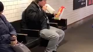 Guy drinks milk and pours cereal into his mouth in subway station