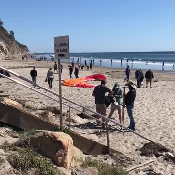 Orange parachute guy tries to run across beach