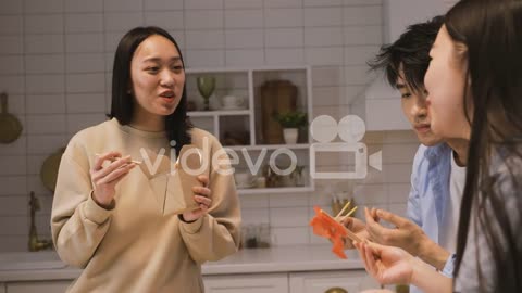 Three Japanese Friends Sitting Around The Kitchen Counter And Eating Japanse Food