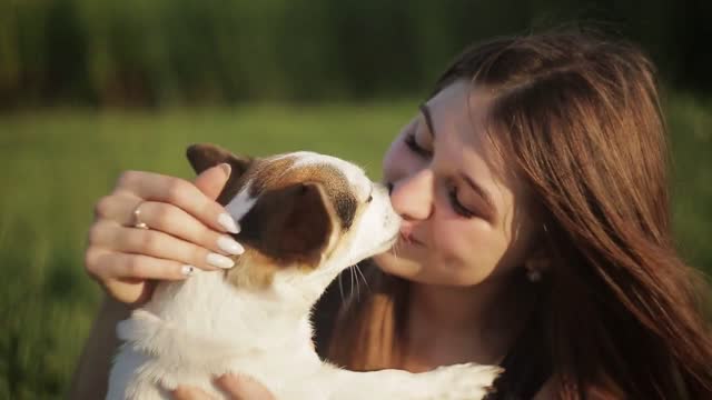 A girl and a dog are kissing in nature She carry on a dog