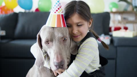 A Girl Kissing a Dog Wearing a Party Hat