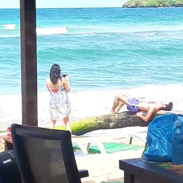 Girl taking picture for guy in blue shorts laying on rocks