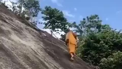A monk climbing with bare feet on the cliff that tourists climb on with the help of a rope ...