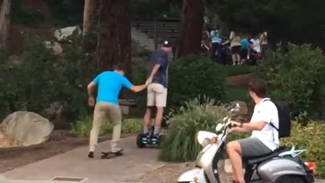 Guy on hoverboard helping guy on skateboard