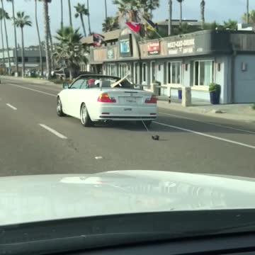 White car with white surf board dragging string