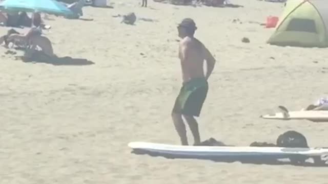 Man in green shorts on the beach does stretches