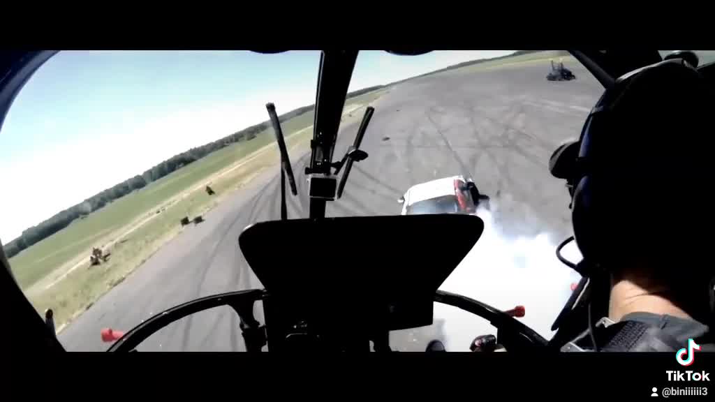 Drifting racing car is pursued by an aerobatic helicopter.