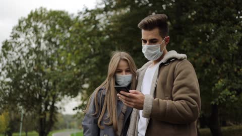 A Couple Wearing Face Mask While Watching on Mobile Phone