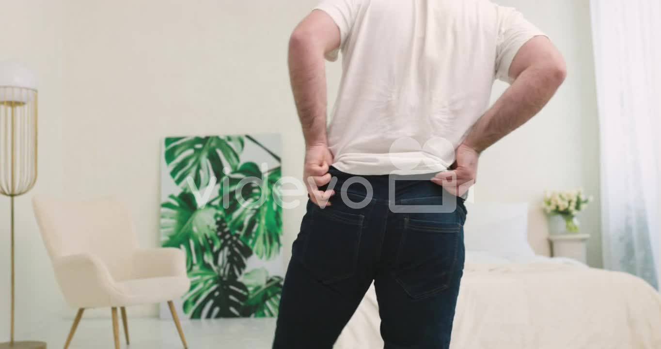 Rear View Of Man Buttoning Tight Jeans With Difficulty In The Bedroom