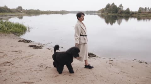 A charming young woman in a stylish white coat goes along the river bank