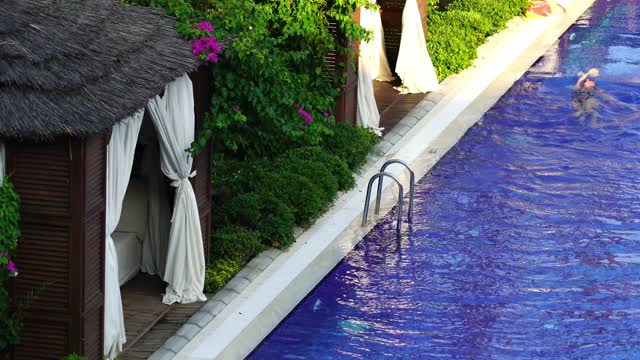 Woman Swimming In A Pool Lined With Cabanas