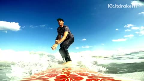 Guy in button down shirt and jeans surfs on a red surfboard