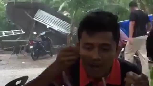 indonesian man eating food while a cyclone behind him happened