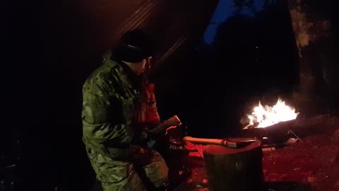 Chopping firewood by the campfire under a tarp at night