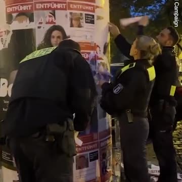 Police in socialist Germany is seen removing posters of Israeli hostages