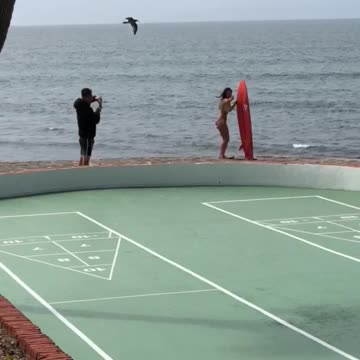Woman in bathing suite poses for picture next to surf board