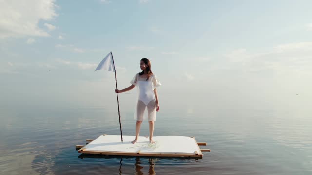 A Woman Holding a White Flag while Standing on the Raft