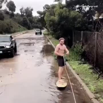 Shirtless guy in black shorts wakeboarding on flooded streets falls immediately