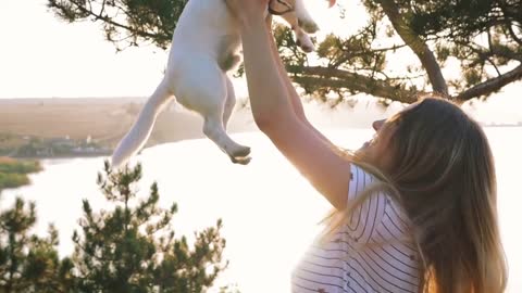 Young attractive woman playing with a dog Jack Russell in the meadow at sunset with sea background