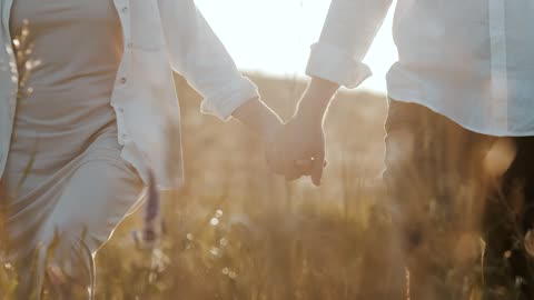 Close up of a happy couple walking through a field hand in hand