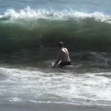 Guy in black shorts gets knocked down by wave