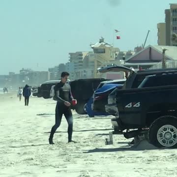 Guy wearing wetsuit walking back to truck with red cup in hand