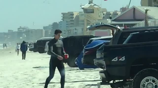 Guy wearing wetsuit walking back to truck with red cup in hand