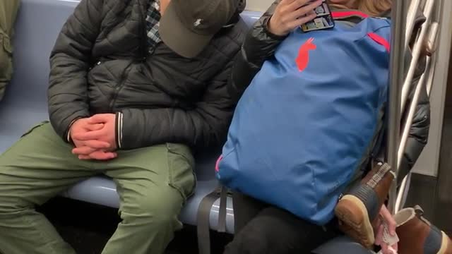 Man falls asleep on woman's shoulder on subway train, woman makes funny face