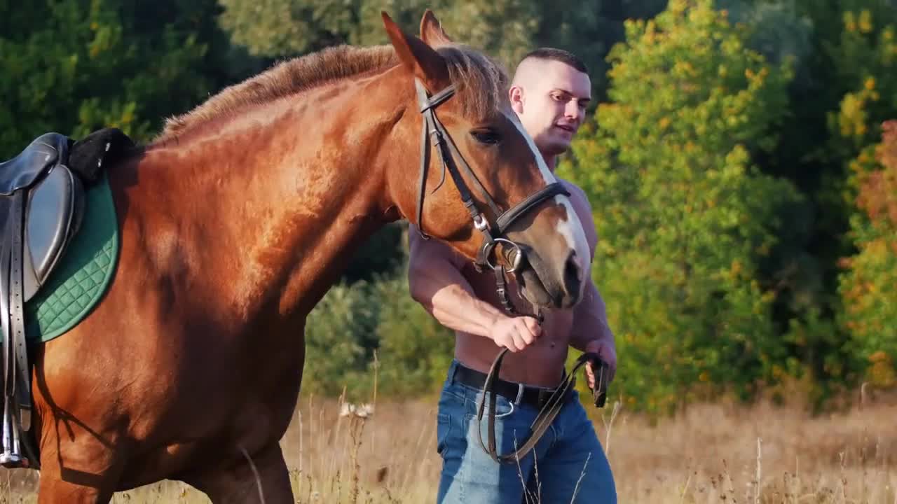 A young man weightlifter walking on the field, next to him is a beautiful horse