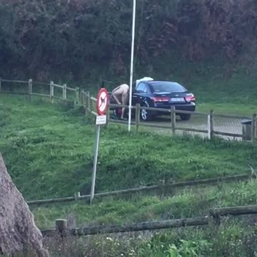 Naked man changing next to black car