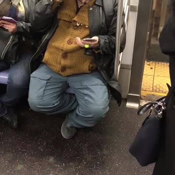 Guy wears bowler cap and bright shiny glasses on train