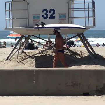 Music white helmet guy carries surfboard on head on beach